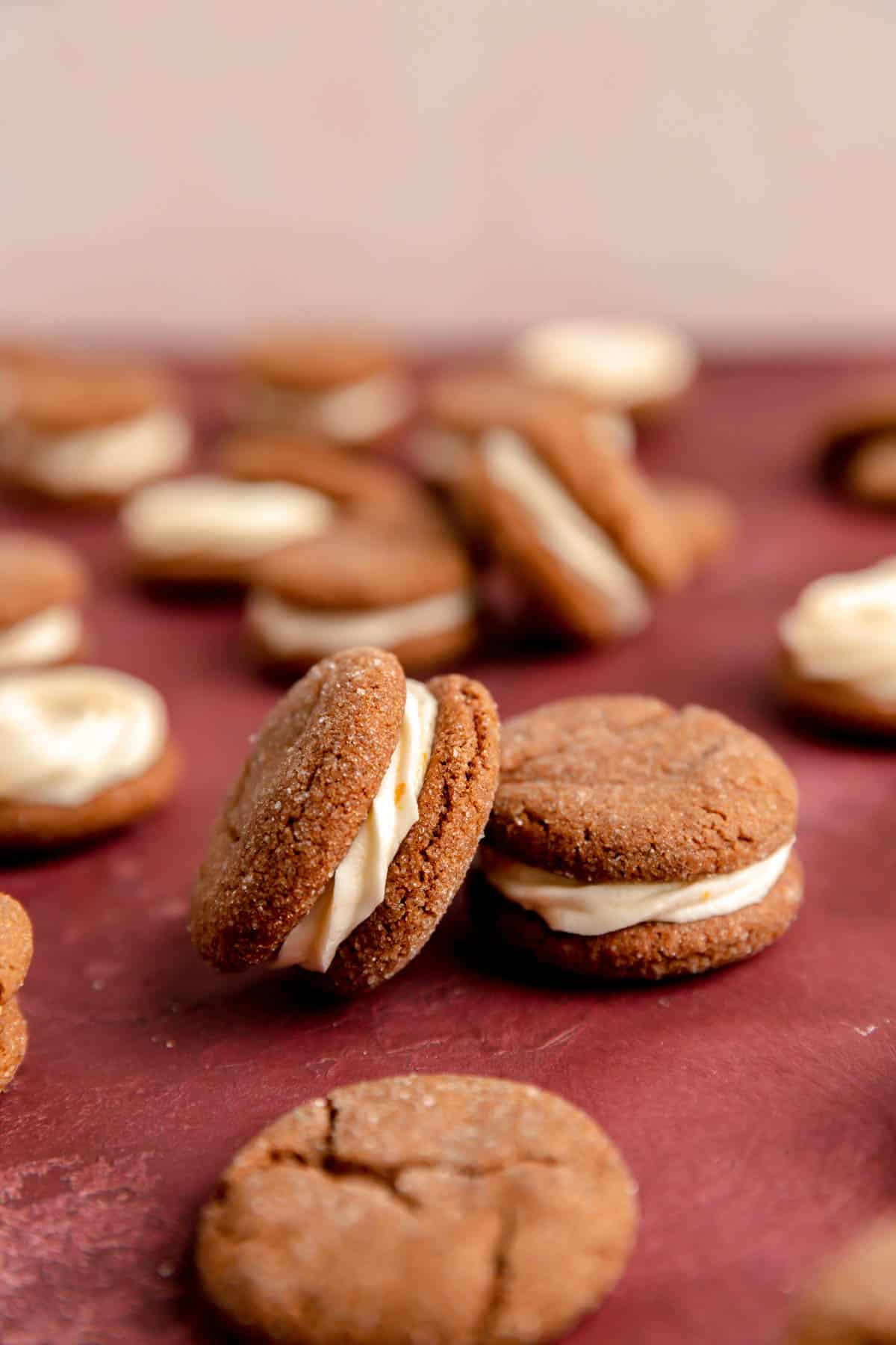 Ginger cream sandwich cookies with one leaning on its side and others scattered in the background