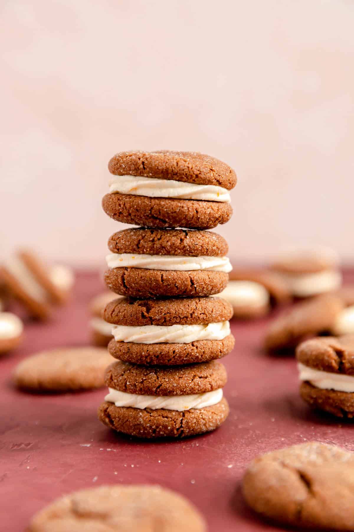 A stack of four ginger sandwich cookies and a burgundy surface with other cookies on the table