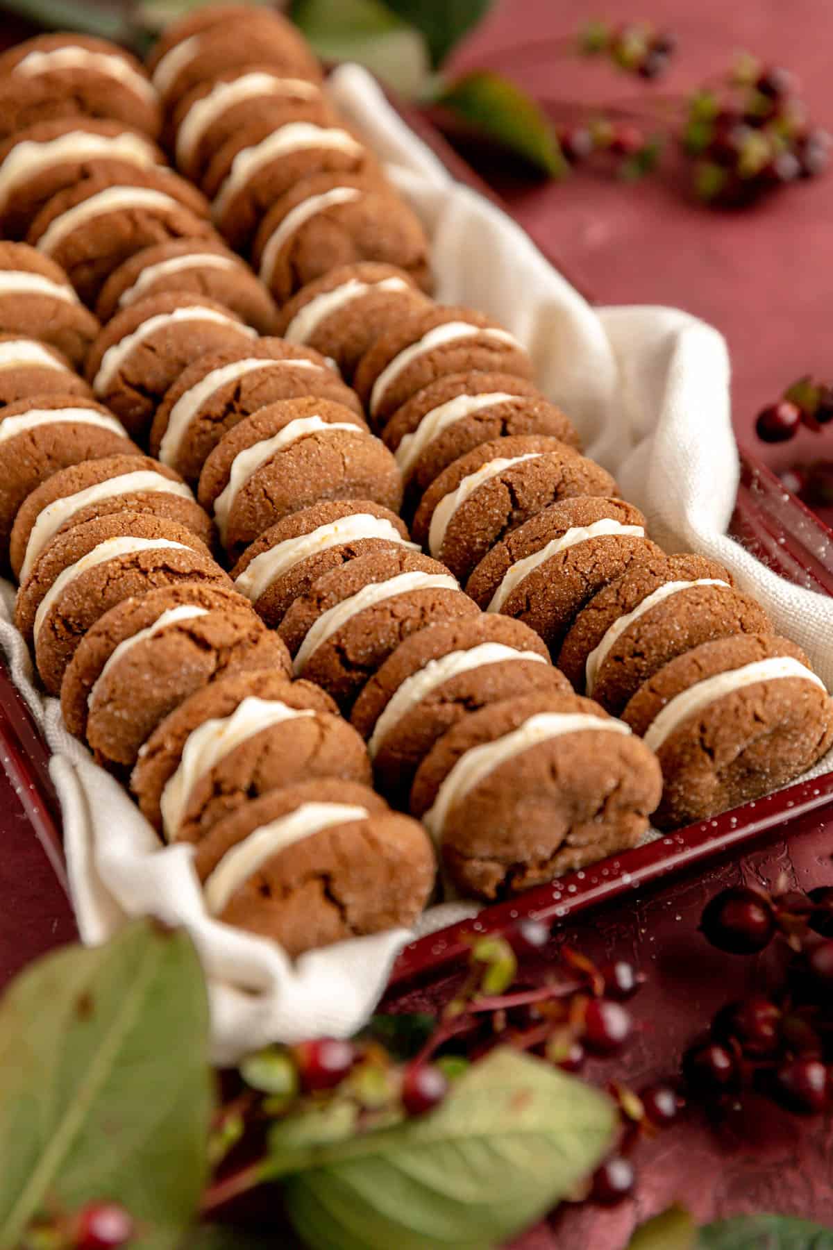 Shot of ginger creme sandwich cookies stacked on a white women with red berries on a red surface