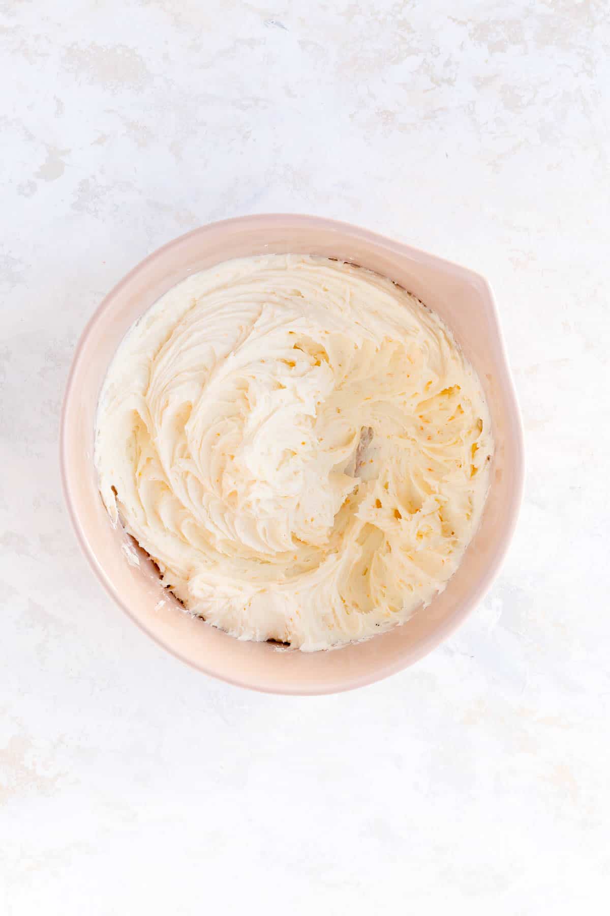 Orange cream frosting fully mixed in with in a brown bowl on a white background