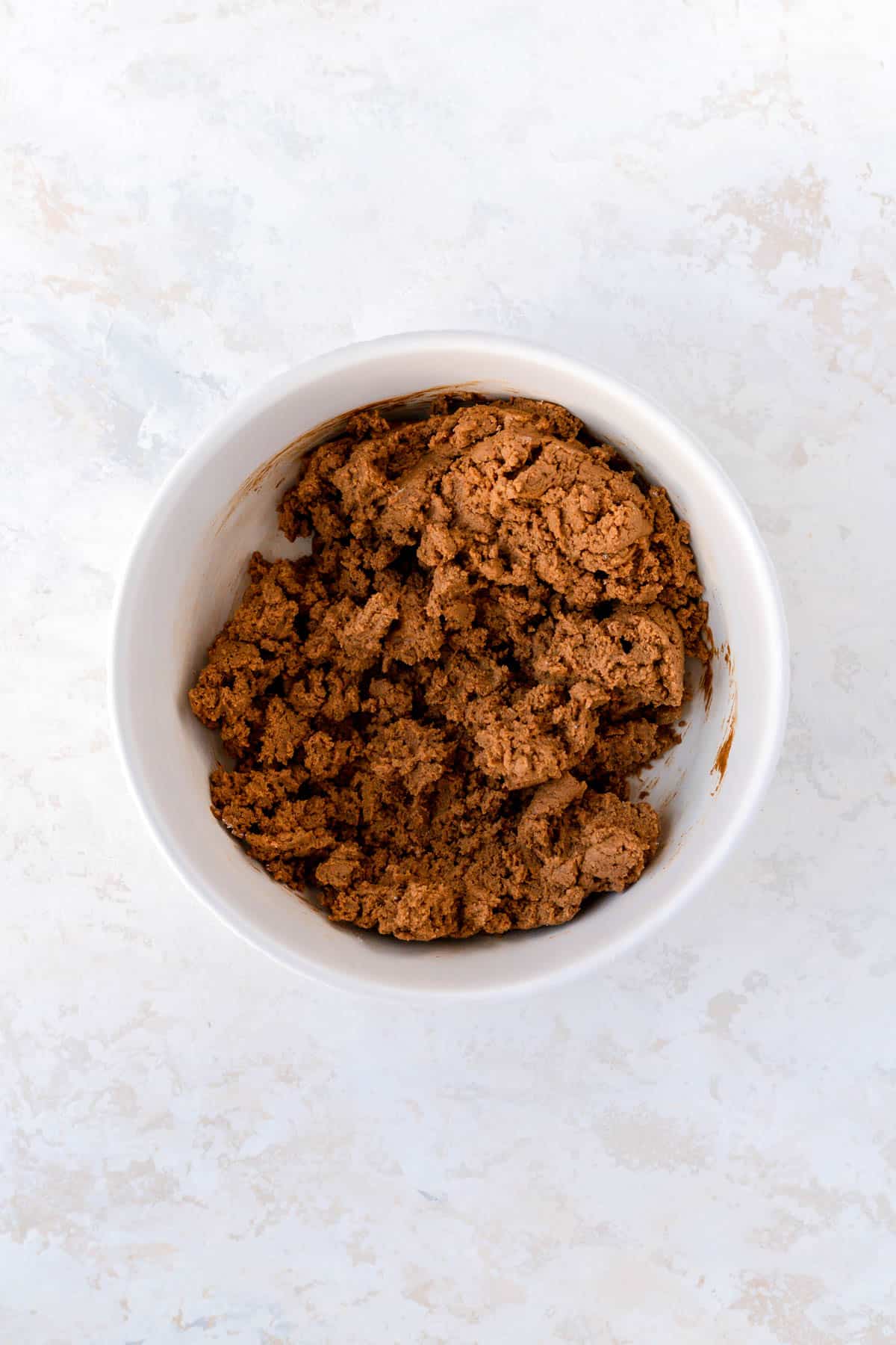 Fully mixed ginger cookie dough in a white bowl on a plaster background