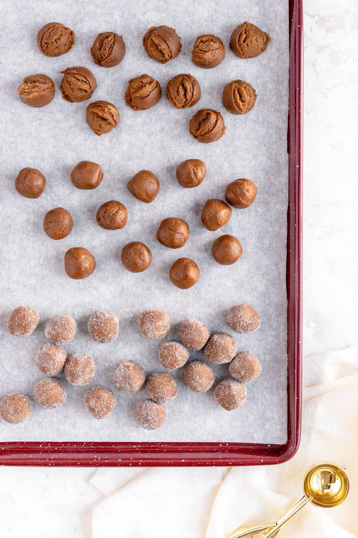 scooped, rolled, and sugar-coated ginger cookie dough balls on a red baking sheet