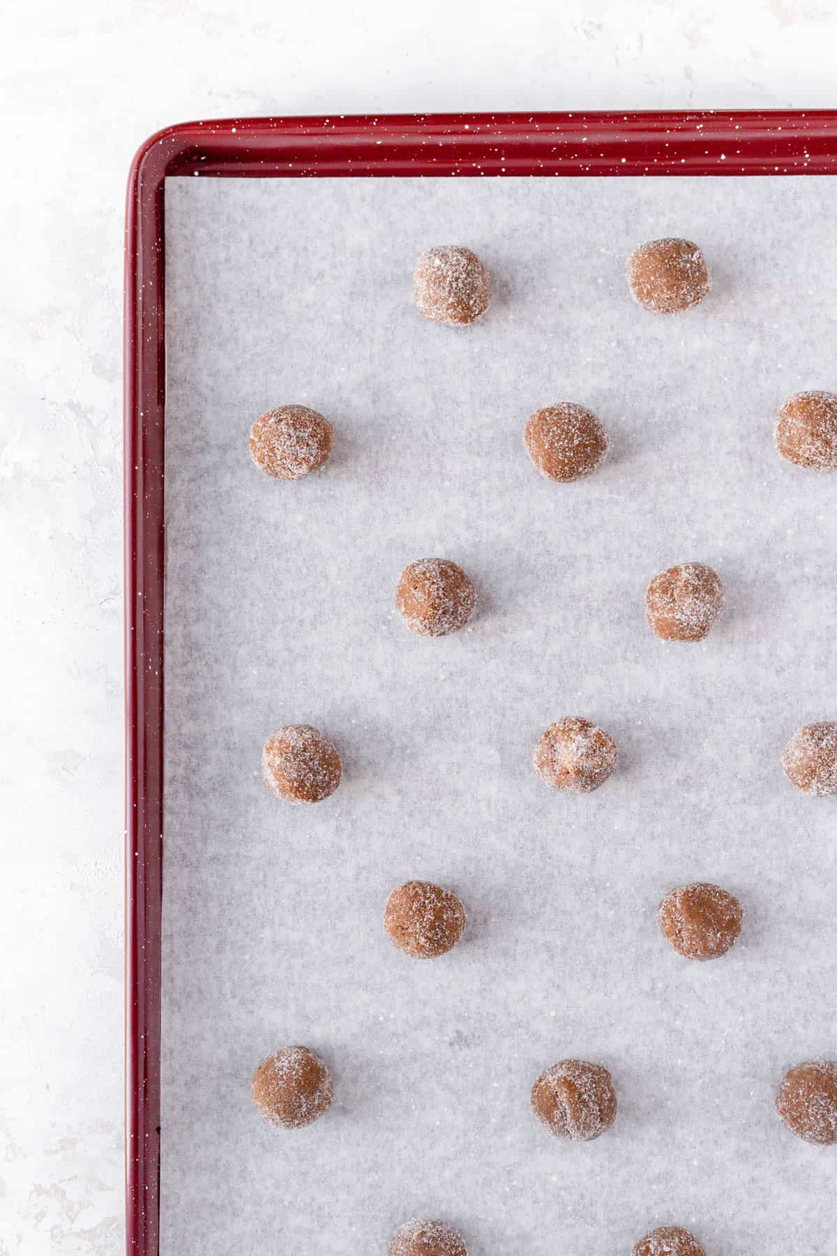 Ginger spice cookie dough balls coded in sugar and parchment paper on a red baking sheet