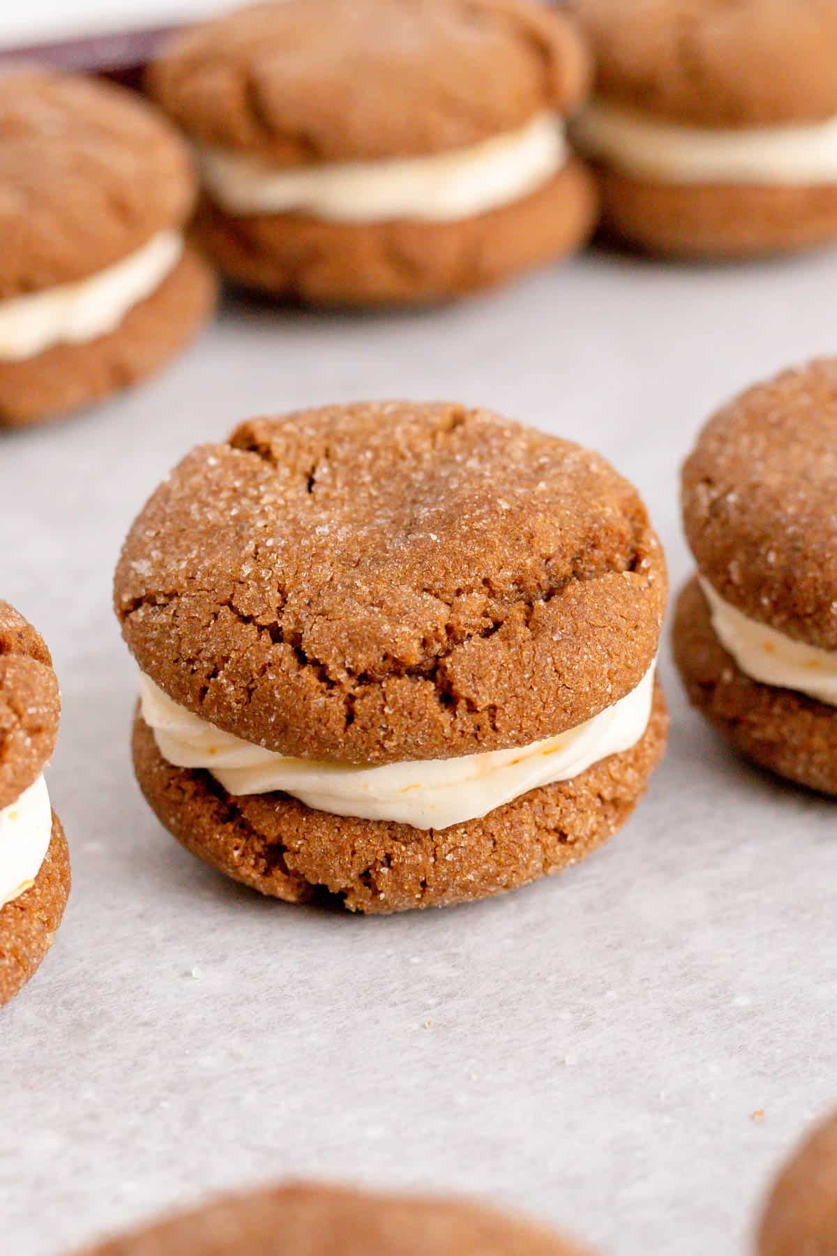 A close-up of a ginger cookie sandwich filled with orange cream frosting on parchment paper
