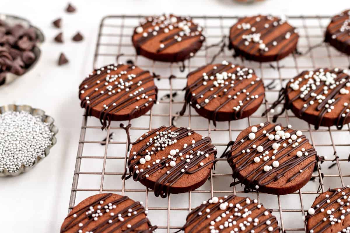 decorated chocolate butter cookies on a metal cooling rack covered in drizzled chocolate.