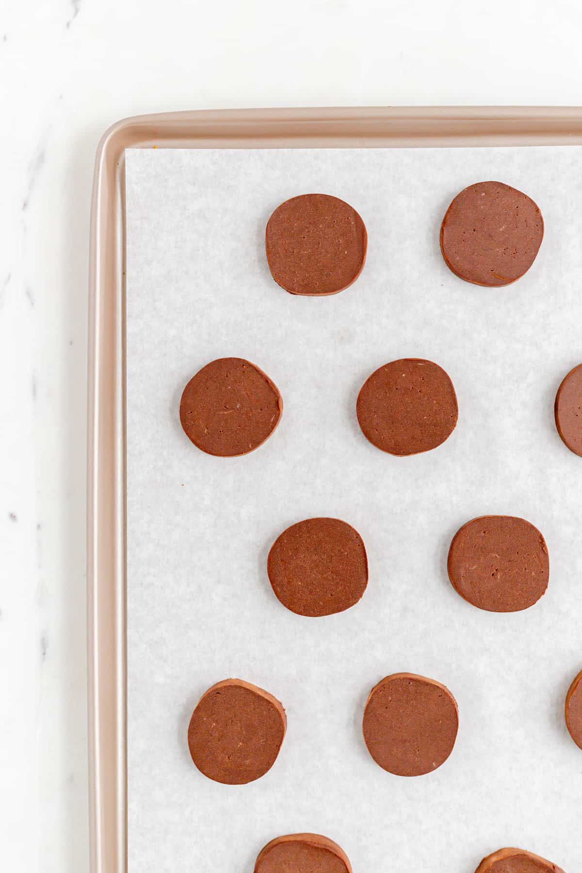 Butter cookie dough slices on a gold sheet pan on a white marble table