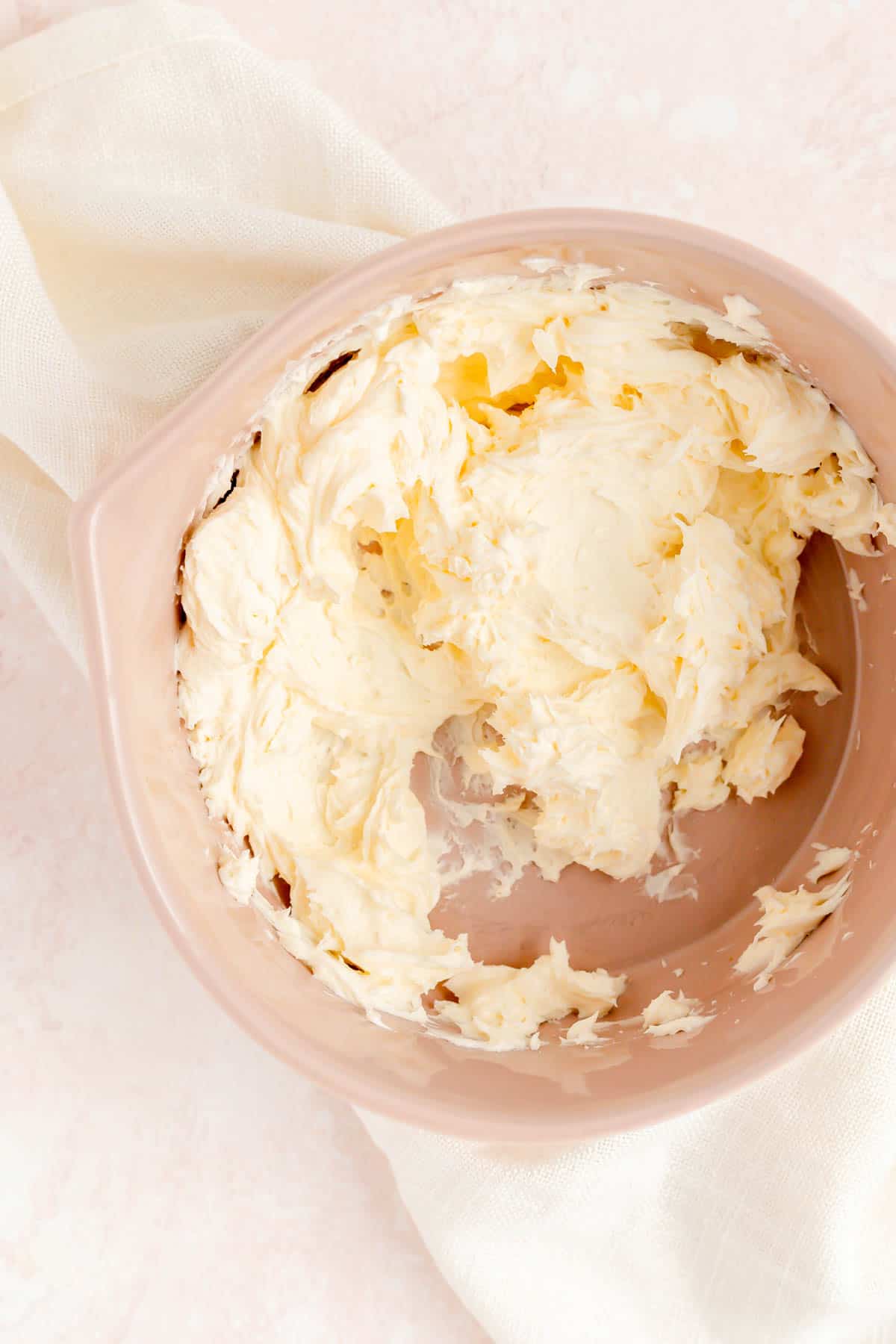 Light and fluffy whipped butter and powdered sugar in a brown bowl on a pink background.