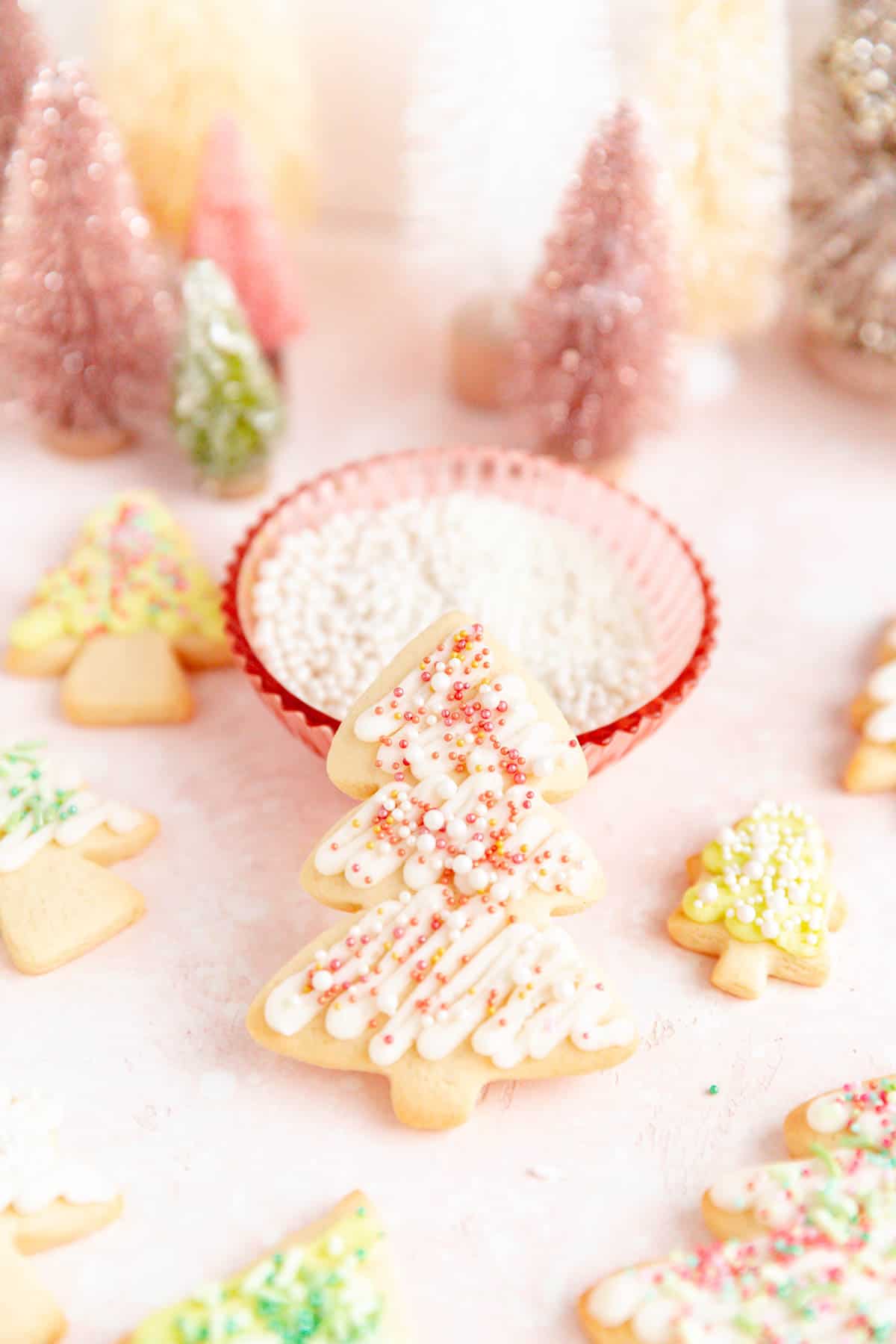 A close-up of a white and pink decorated sugar cookies leaning on a pink bowl of sprinkles