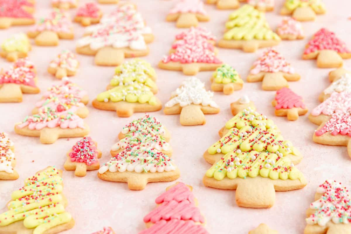Pink green and white decorated tree sugar cookies on a pink background from a side angle