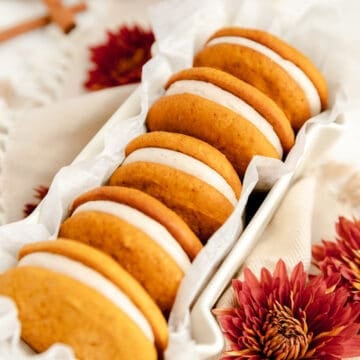 5 pumpkin whoopie pies on their sides in a long white ceramic dish with red mums