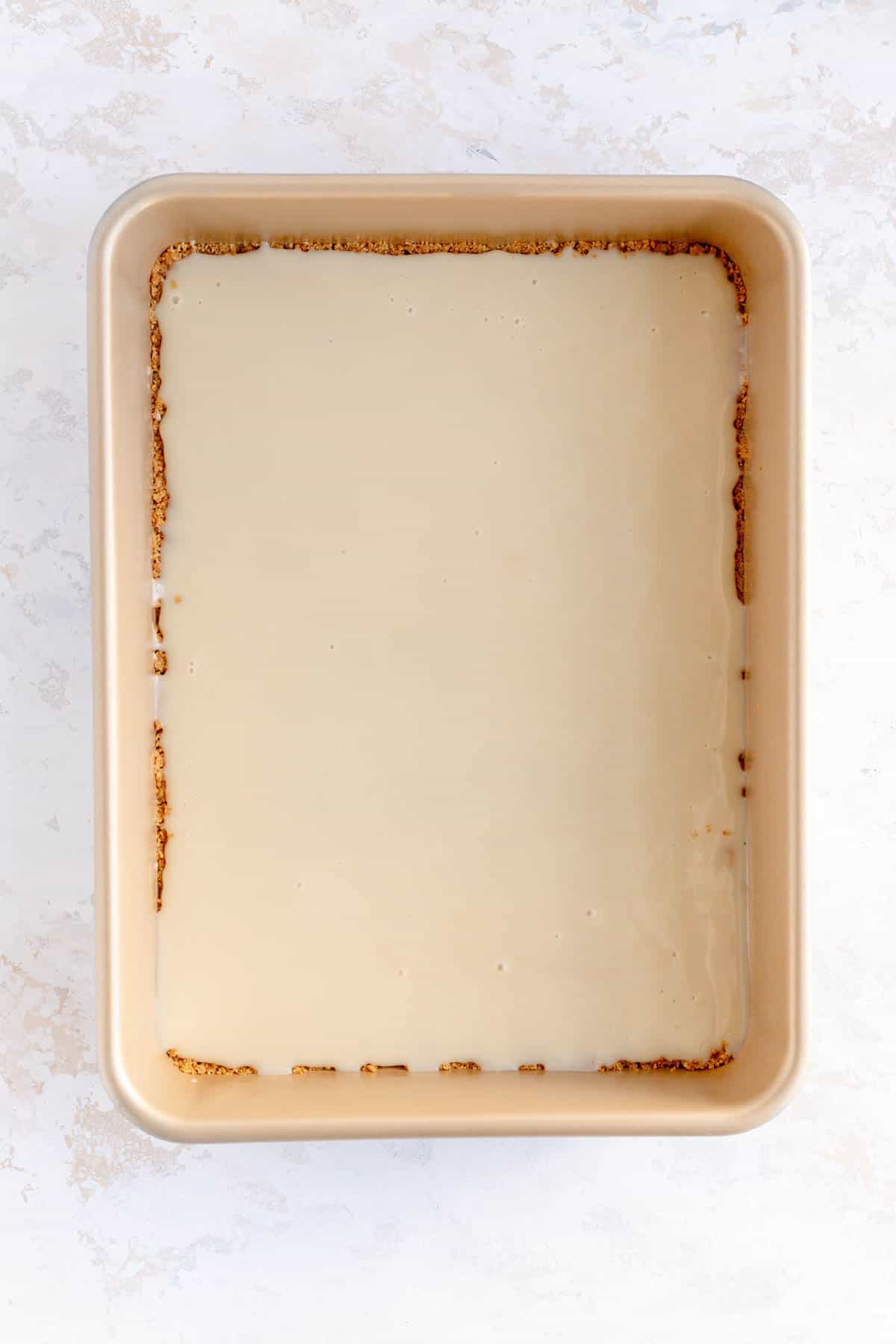 Solid layer of condensed milk over a graham crust in a gold 9 x 13 pan