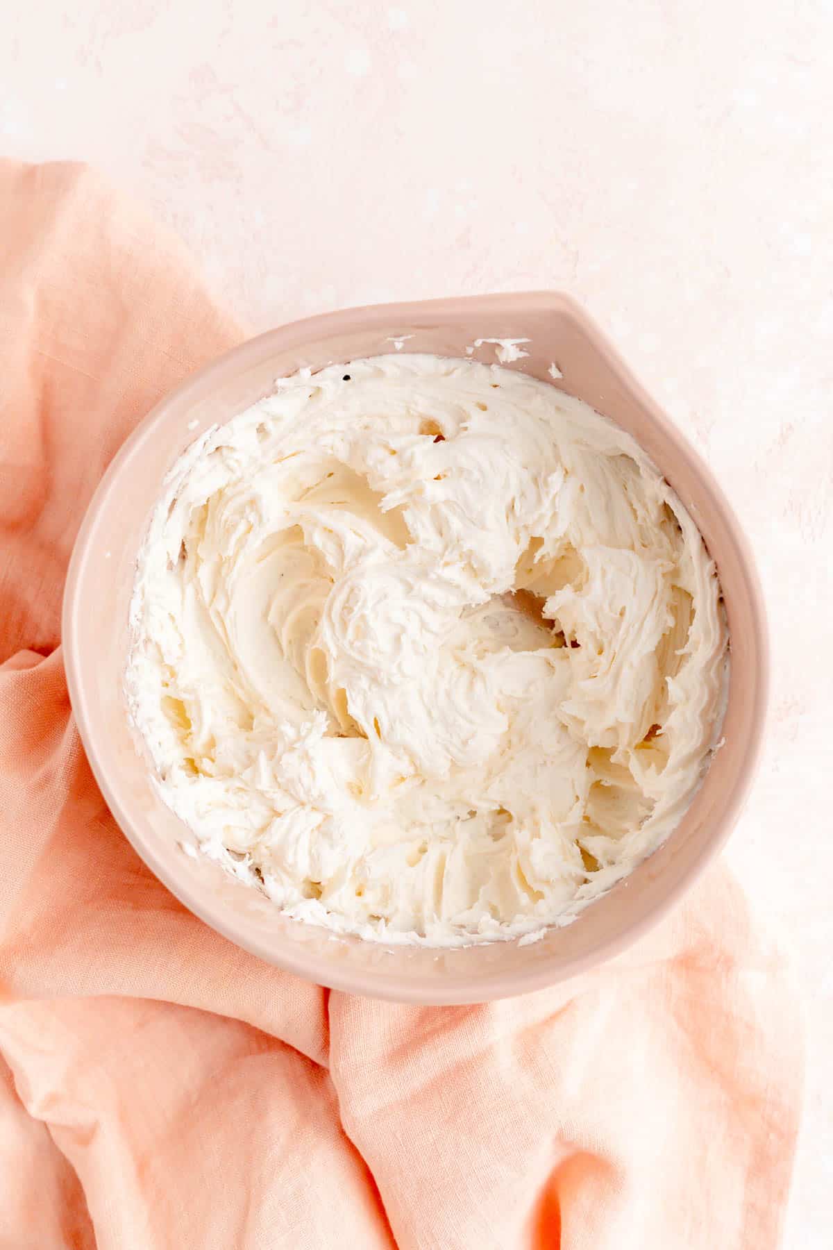 Fully mixed sugar cookie frosting in a white bowl on a pink linen