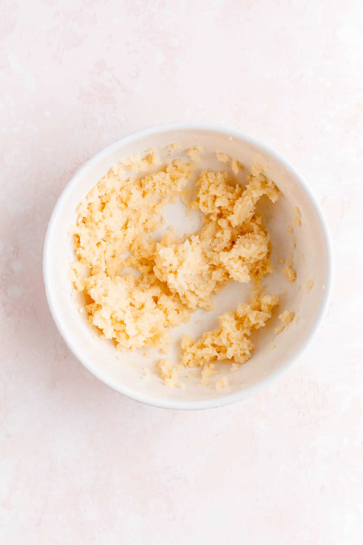 Mixed butter and sugar in a white bowl on a pink background