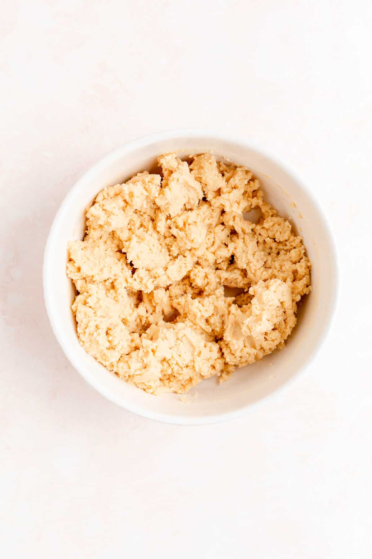 Fully mixed sugar cookie dough in a white bowl and a pink background