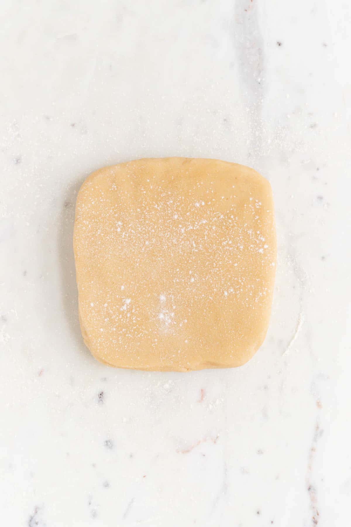 A square block of flowered cookie dough on a white marble surface