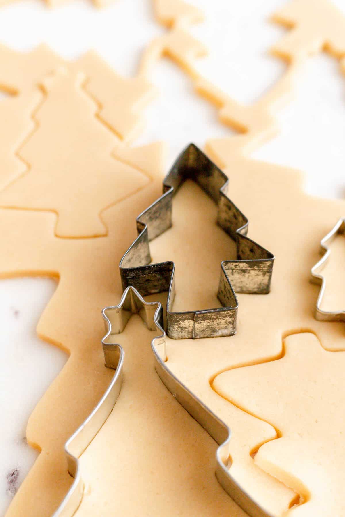 An antique Christmas cookie cutter stuck in cookie dough with other trees cut out around it