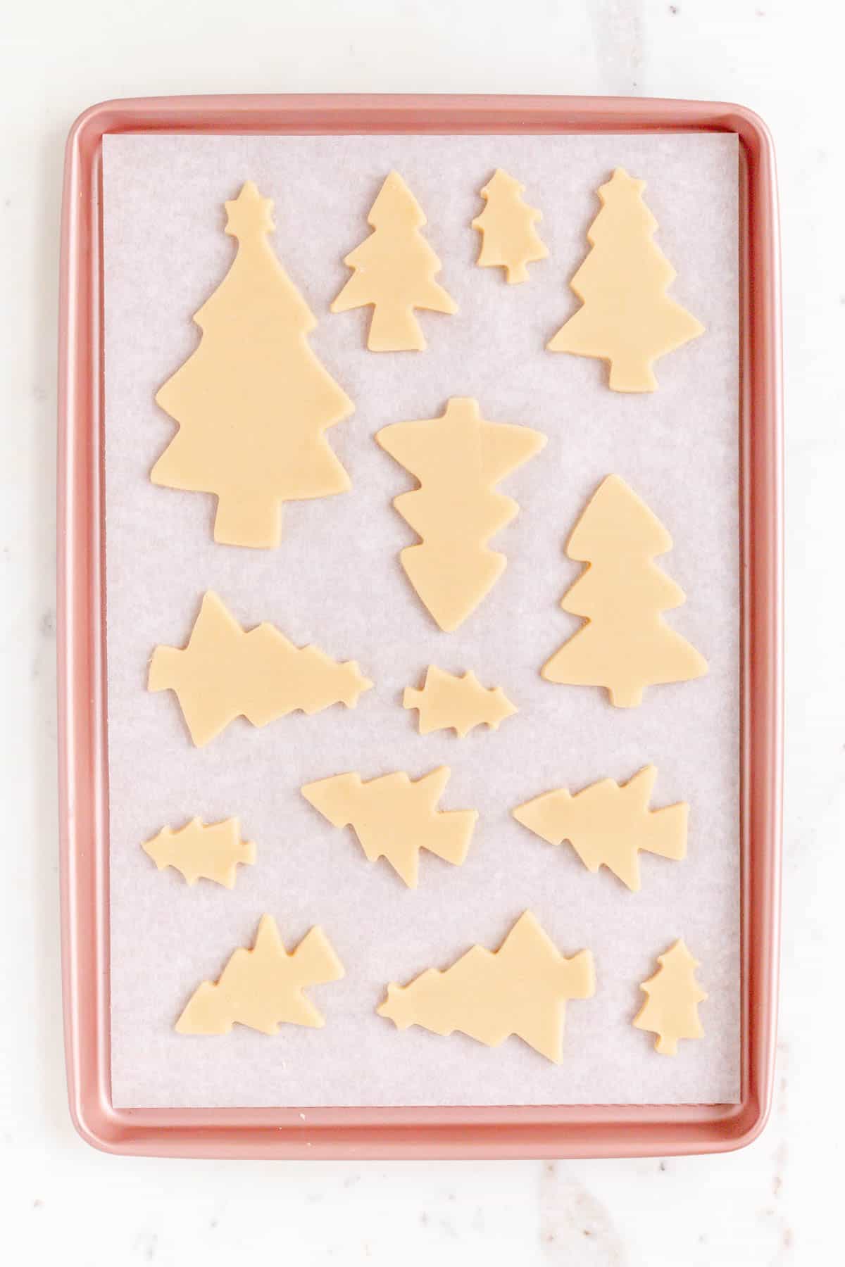 Cut out Christmas tree sugar cookies spaced out on parchment on a pink baking sheet
