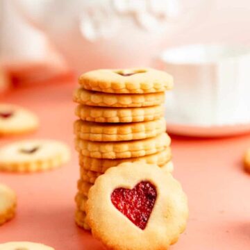 stack of jammy dodgers with one facing the camera and a teapot in the background.