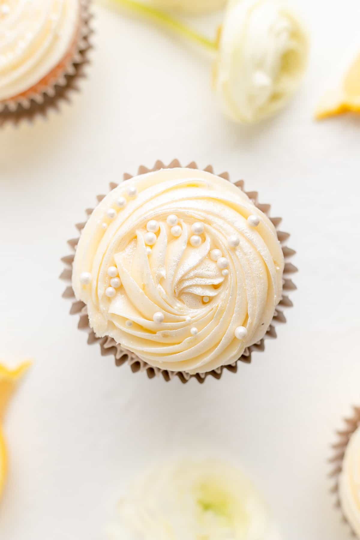 Overhead view of a white cupcake with a rosette pearl spray and white sprinkles with flowers.