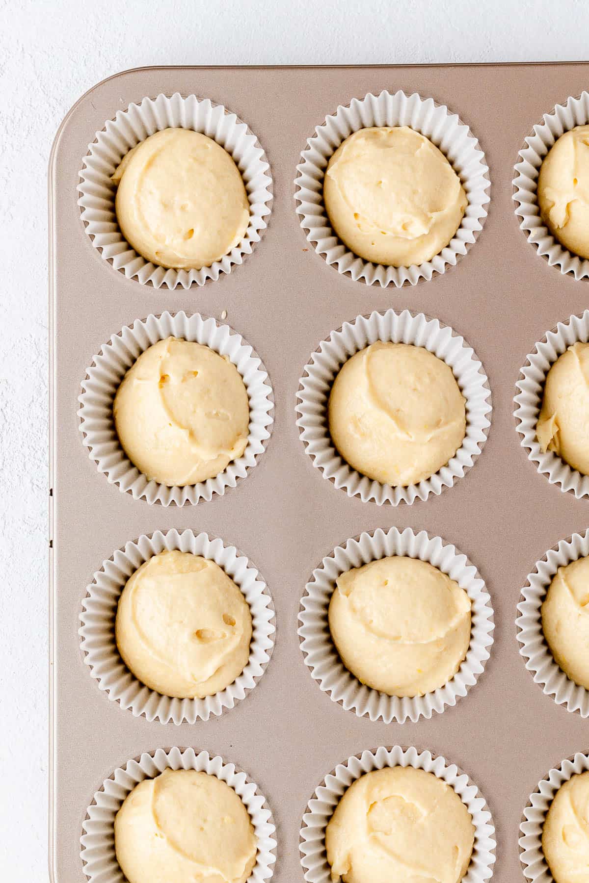 Prosecco cupcake batter in white papers in a gold pan.