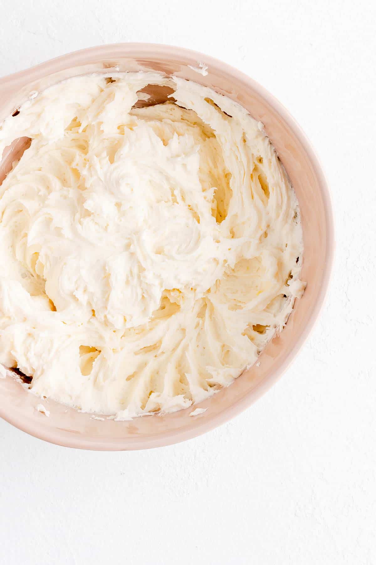 prosecco butter cream whipped in a tan bowl on white background.