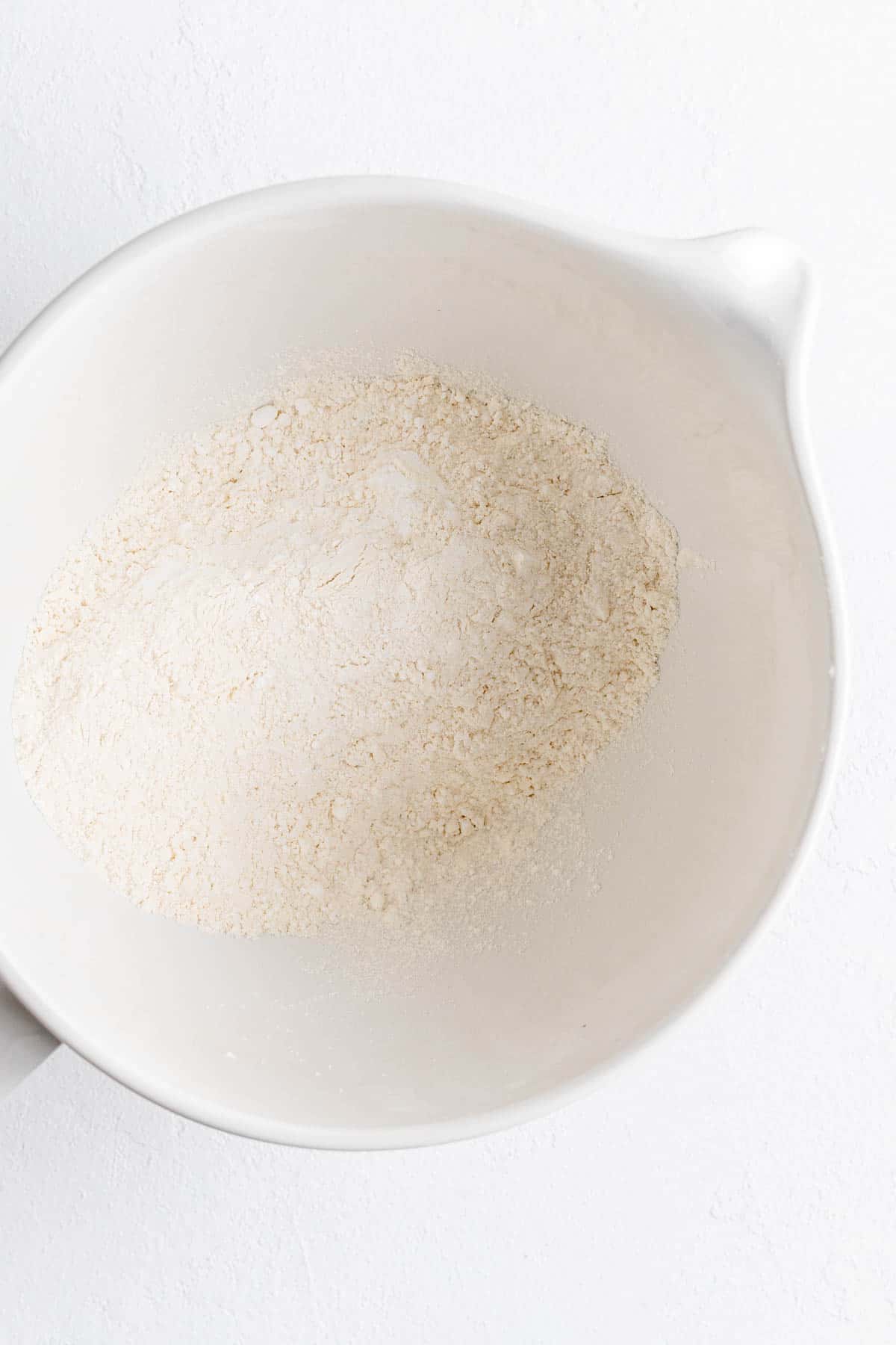 Dry ingredients for shortbread cookie dough in a white mixer bowl on white background.