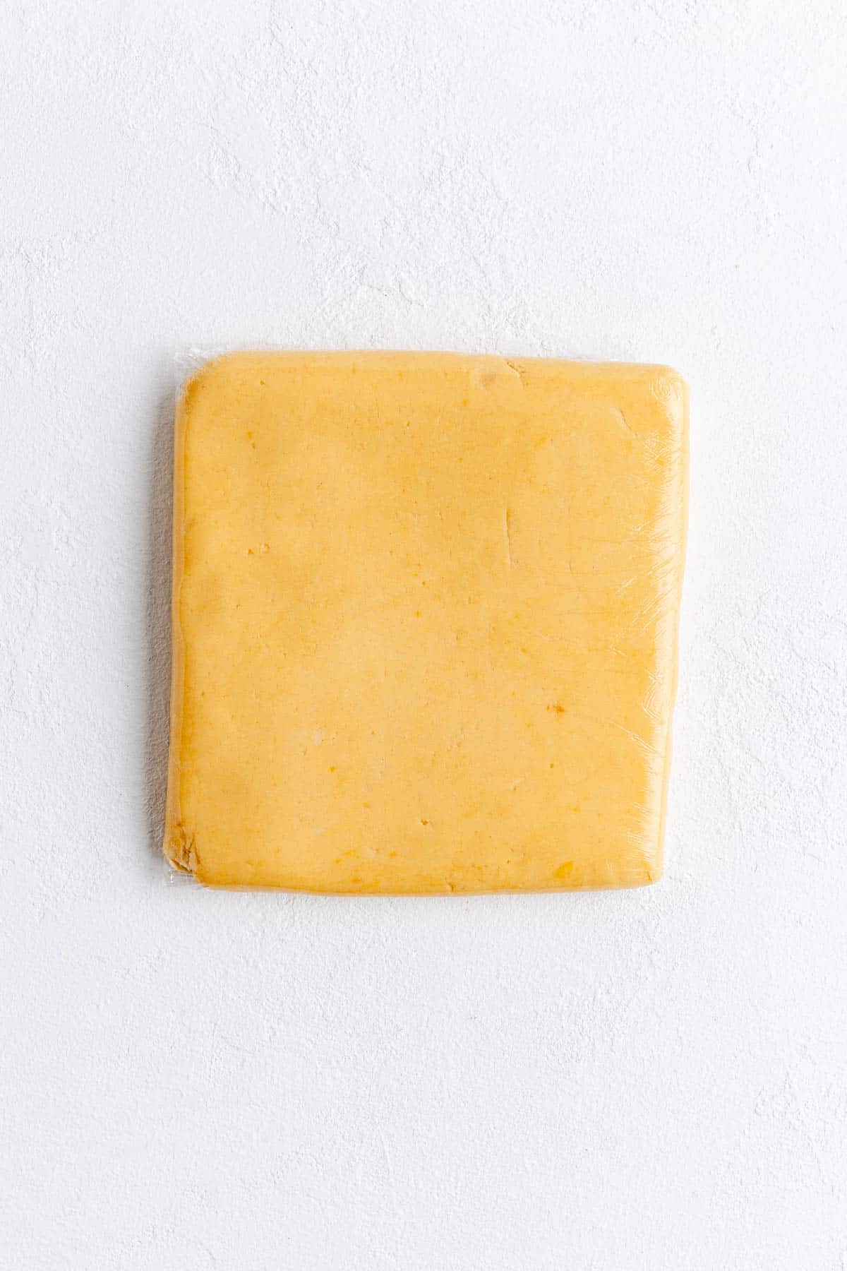 shorbread cookie dough rolled wrapped in plastic wrap in a square shape on white background.