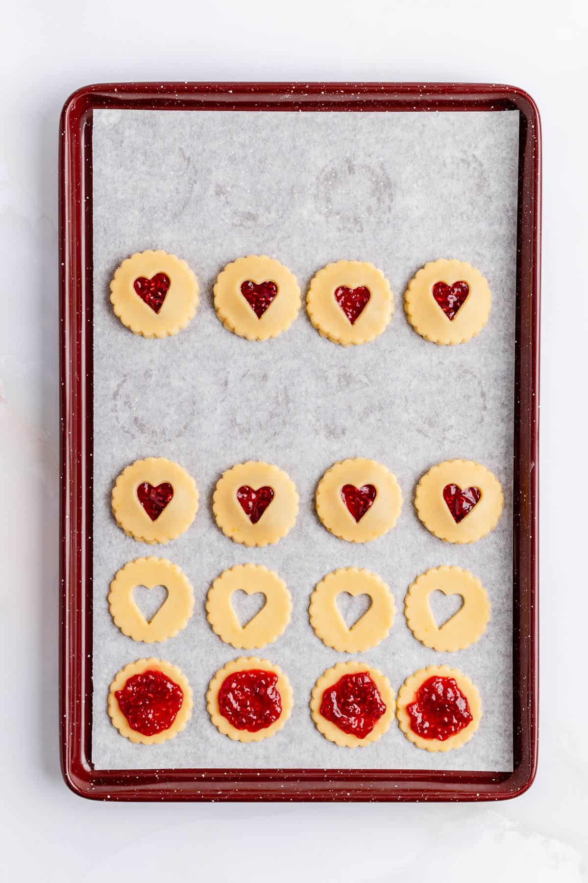 raw jammy dodger cookies filled and unstacked trayed up on parchment paper lined burgundy pan.