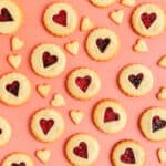 jammy dodger cookies and littler heart cookies scattered on a coral platser surface.