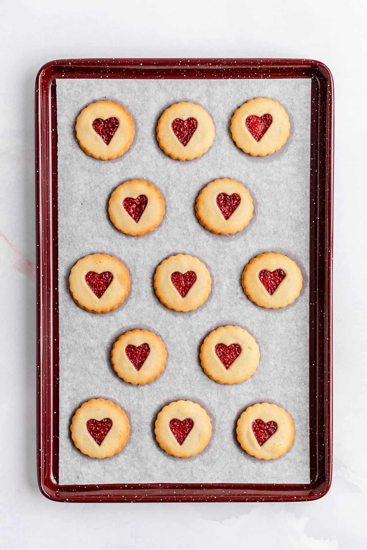 Baked Jammy dodger cookies on parchment on a burgundy pan.