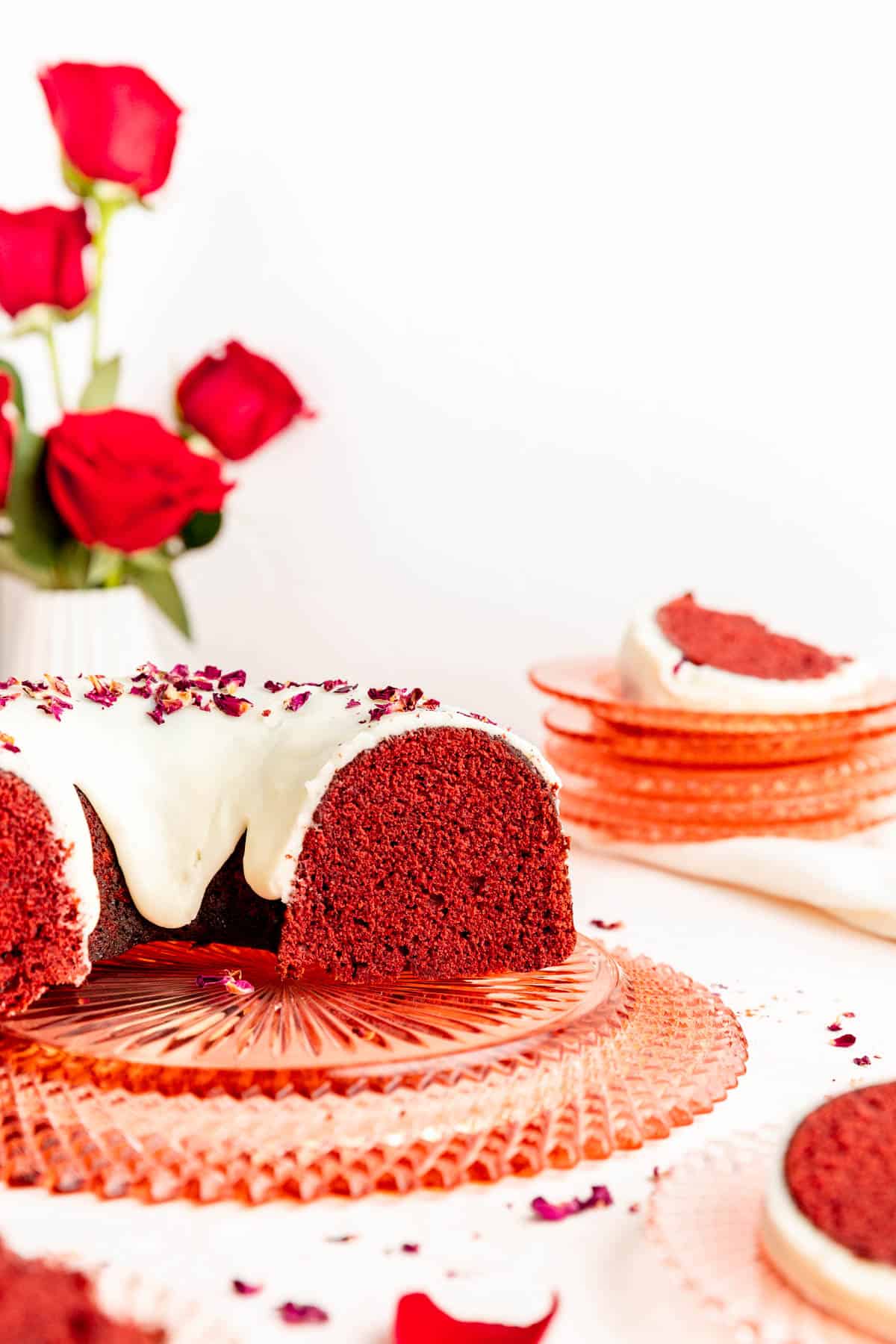 Side view of sliced red velvet Bundt cake with white glaze on pink crystal plate.