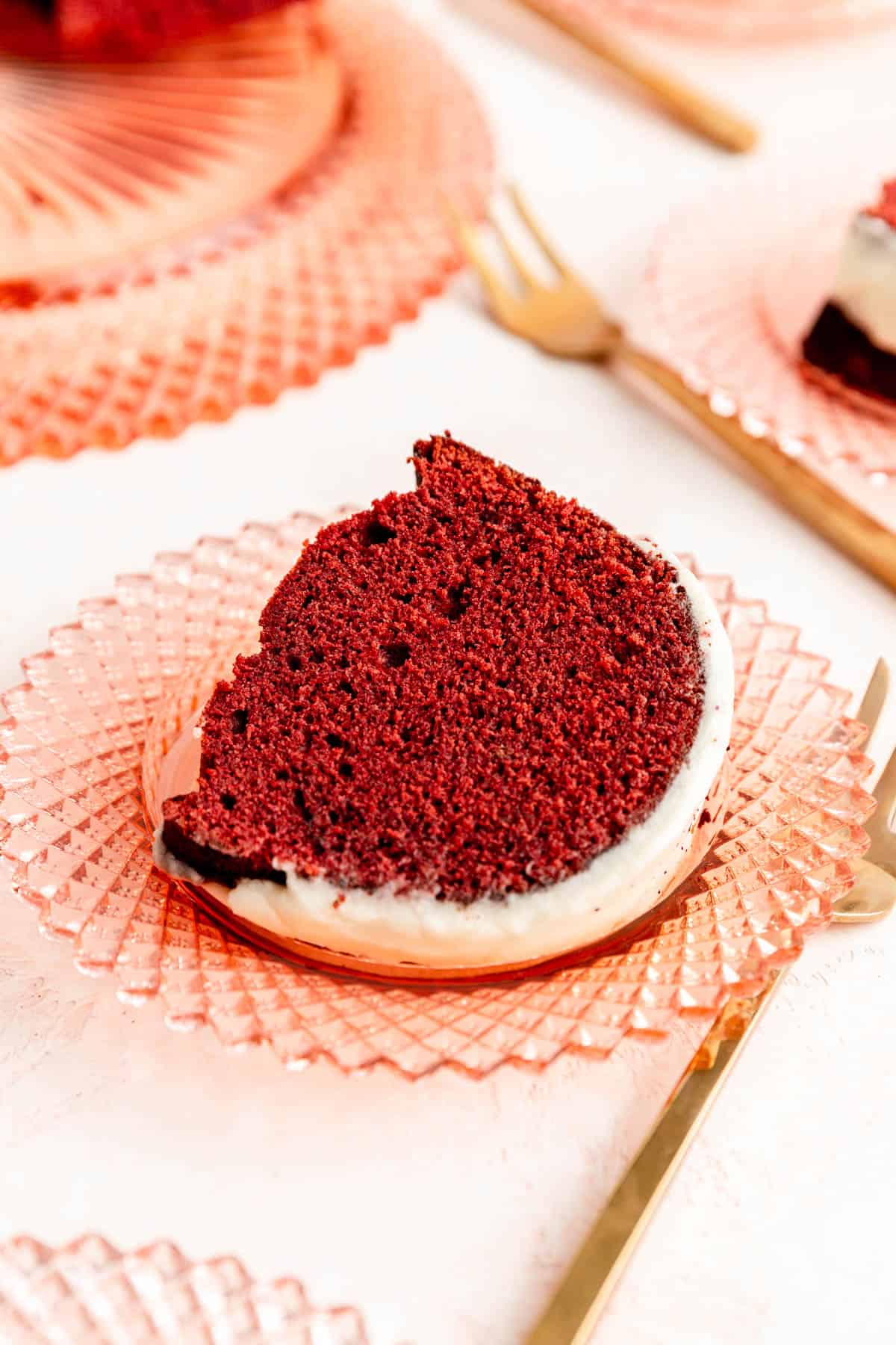 45° view of slice of red velvet Bundt cake with white glaze on pink plate.