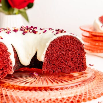 Side view of sliced red velvet Bundt cake with white glaze on pink crystal plate.