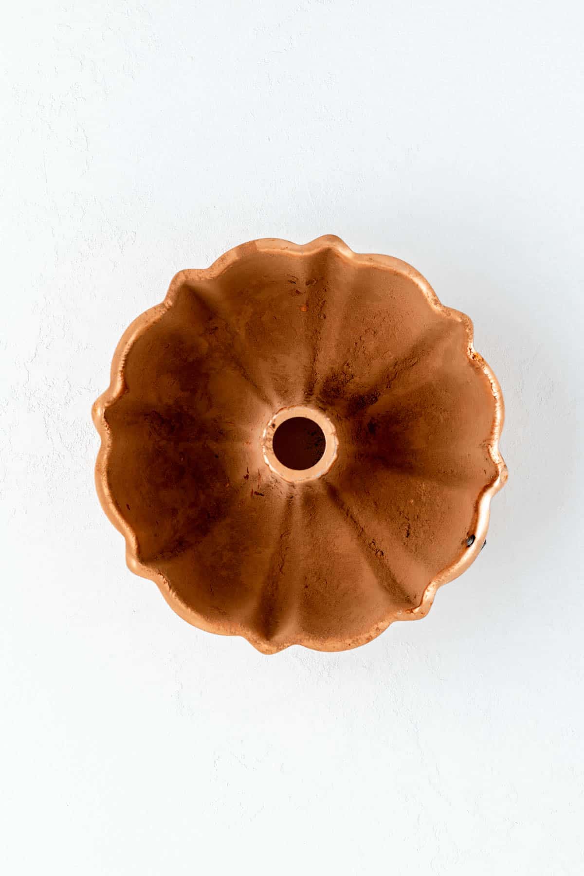 Copper Bundt pan dusted in cocoa powder on white background.