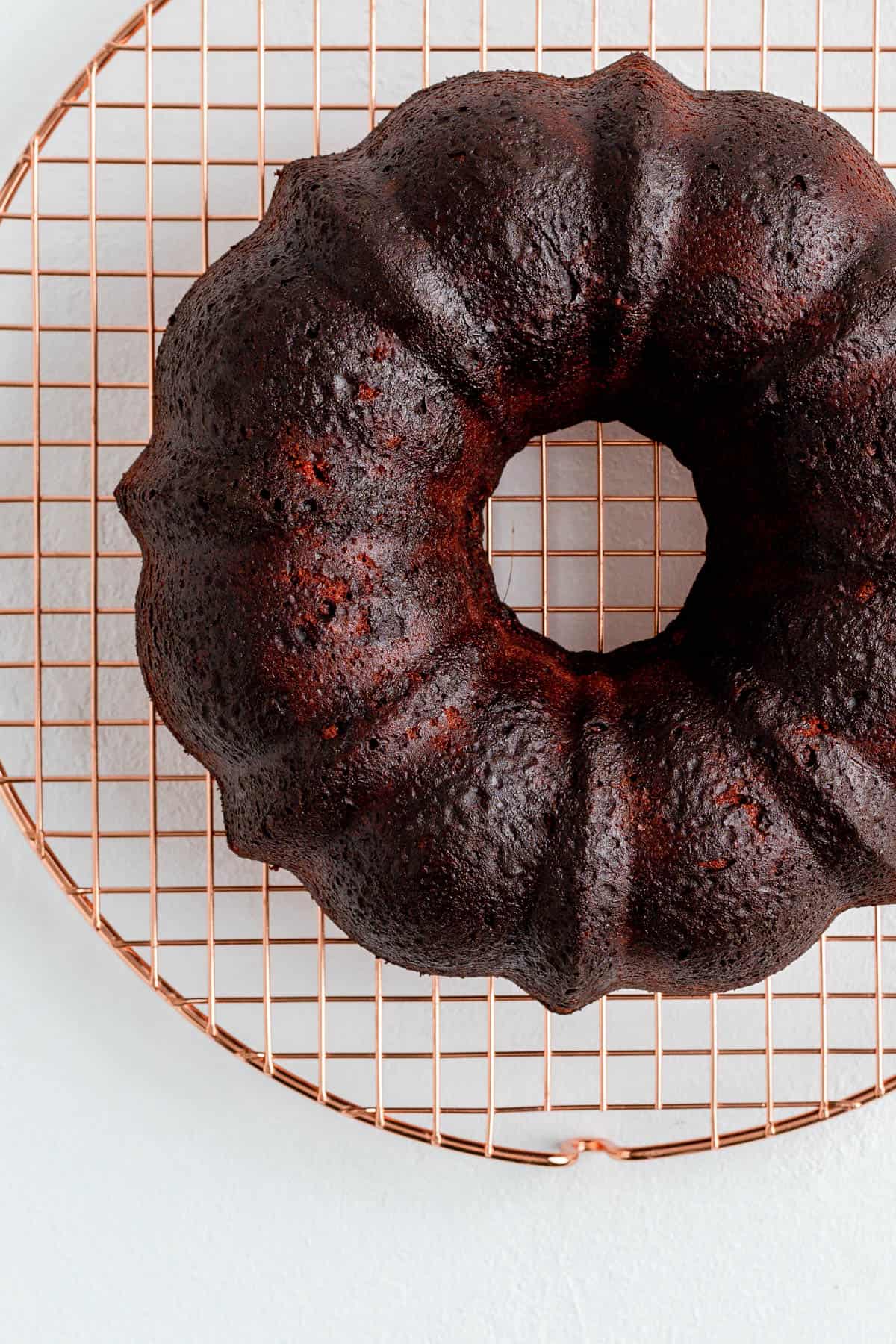 baked Dark brown and red Bundt cake on copper cooling rack on white background.