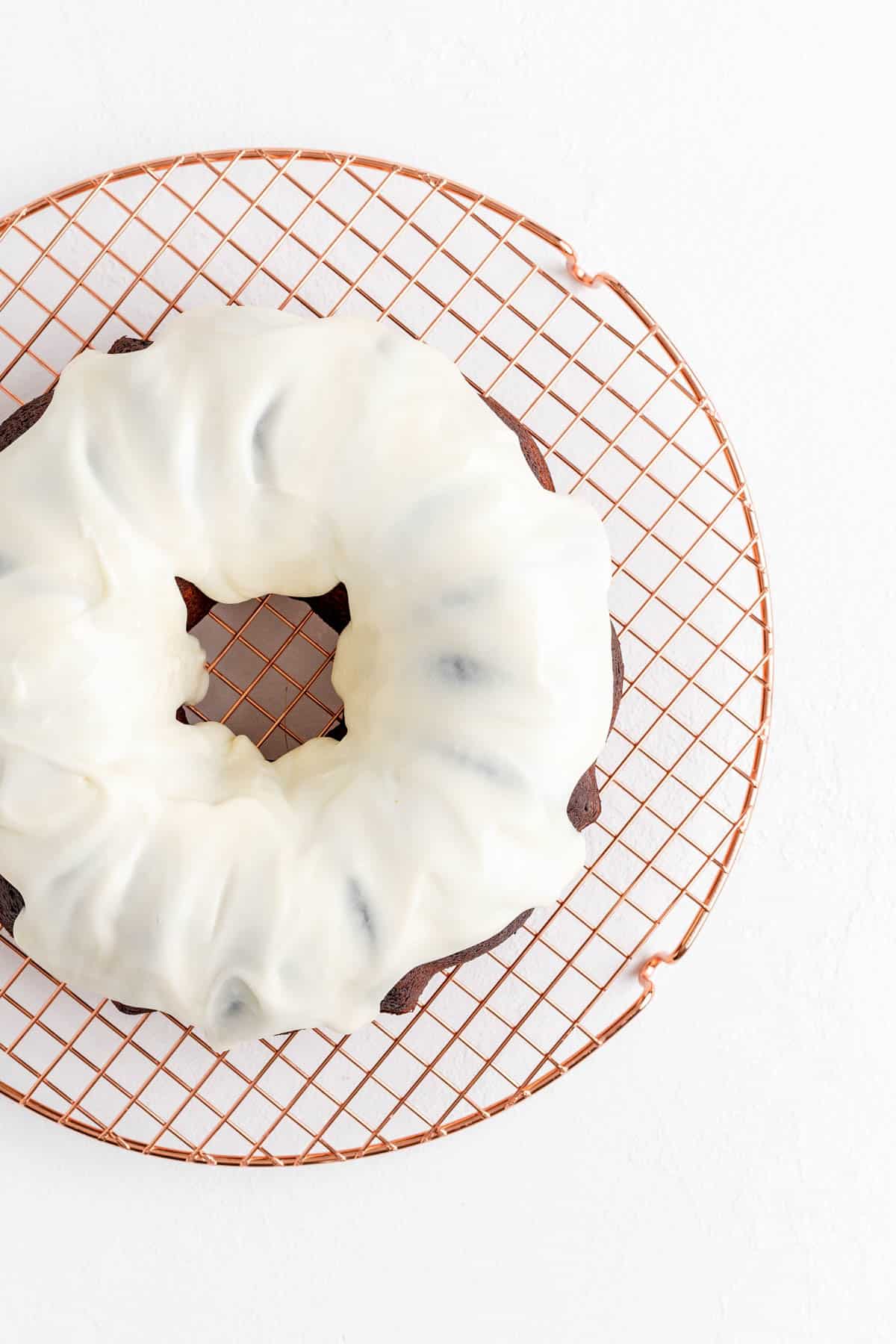 Overhead view of red bundt with white glaze dripping down from top on copper wire rack.