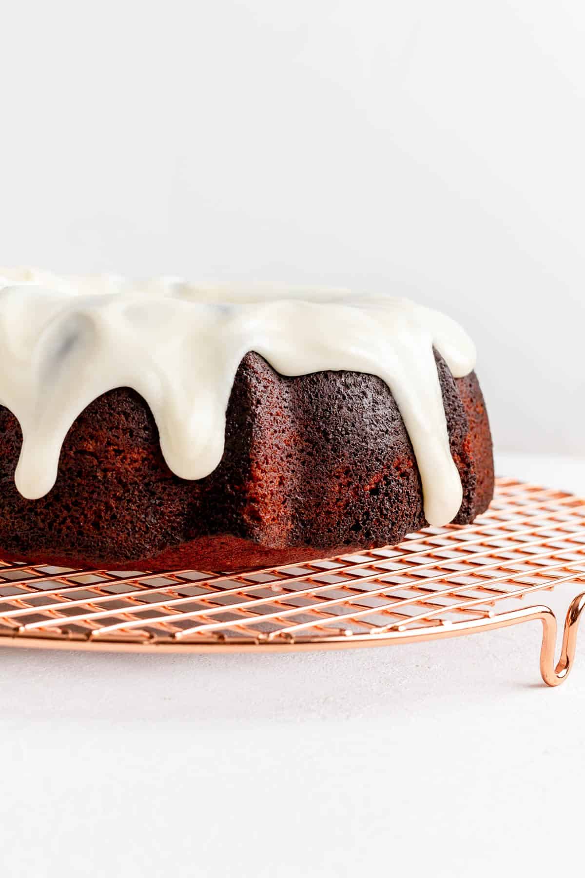 Read Bundt cake on copper cooling rack with white glaze dripping down from top.
