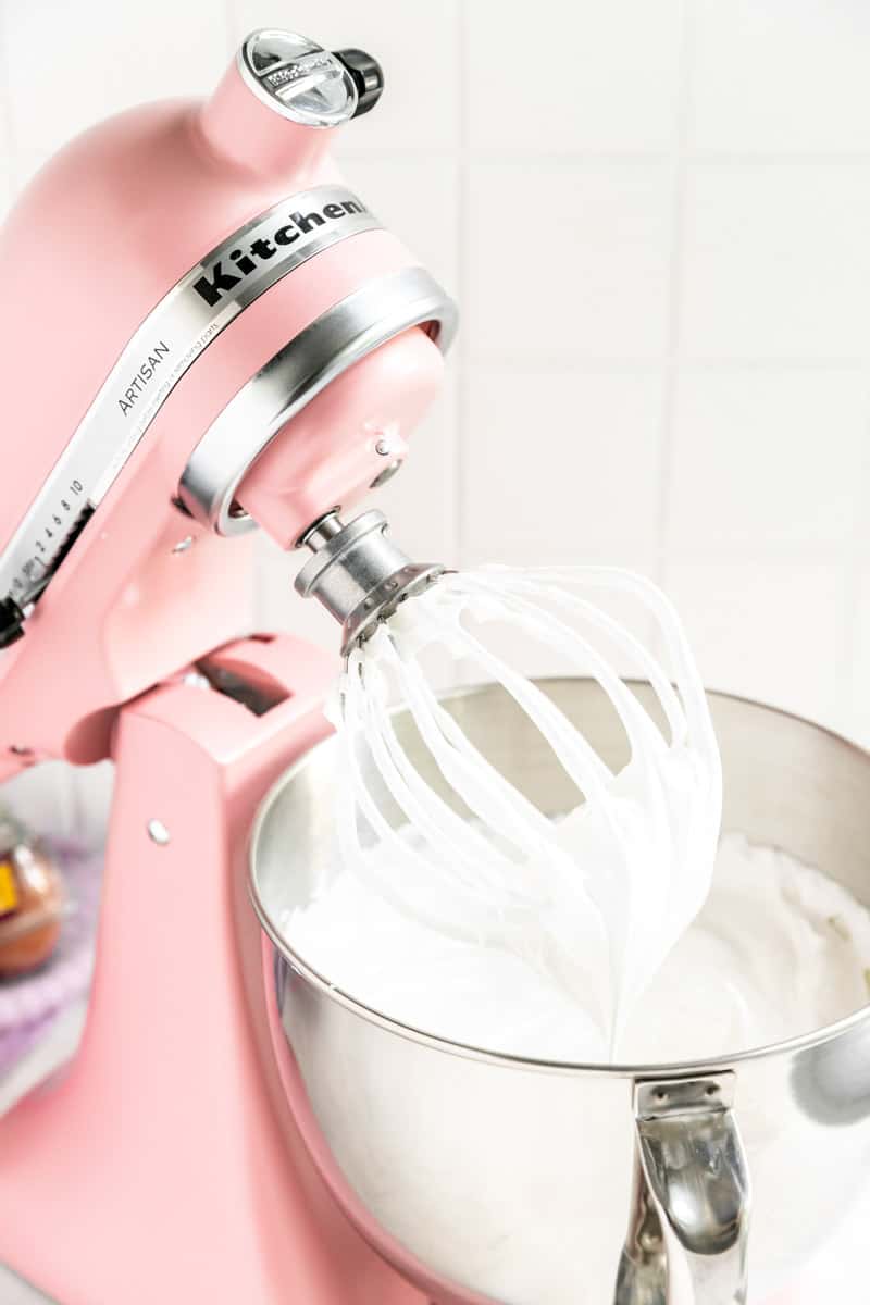 Pink KitchenAid mixer with whisk attachment covered in meringue in stiff peaks.