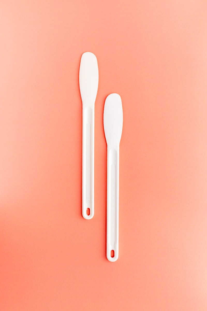 Two white plastic spreader knife on coral background.