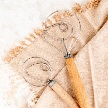 two dough whisks on tan and white chevron towel and white background.