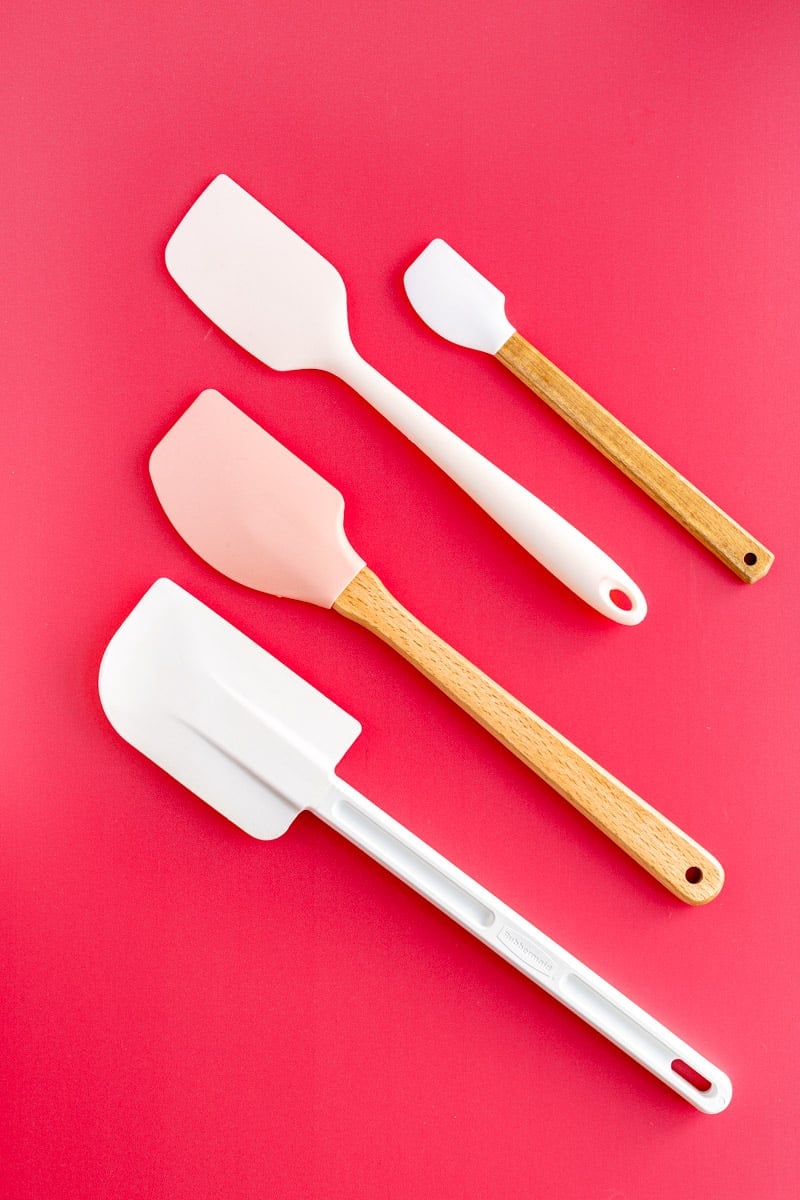 For white wood and pink spatulas lined up on dark pink background.