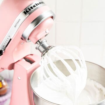 Pink KitchenAid mixer with whisk attachment covered in meringue in stiff peaks.