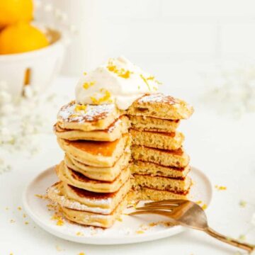 Stack of lemon pancakes with full bite out of the stack and fork on the plate.