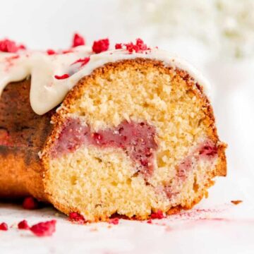 Close up of cross-section of sliced Bundt cake with white chocolate sauce showing raspberry swirl.