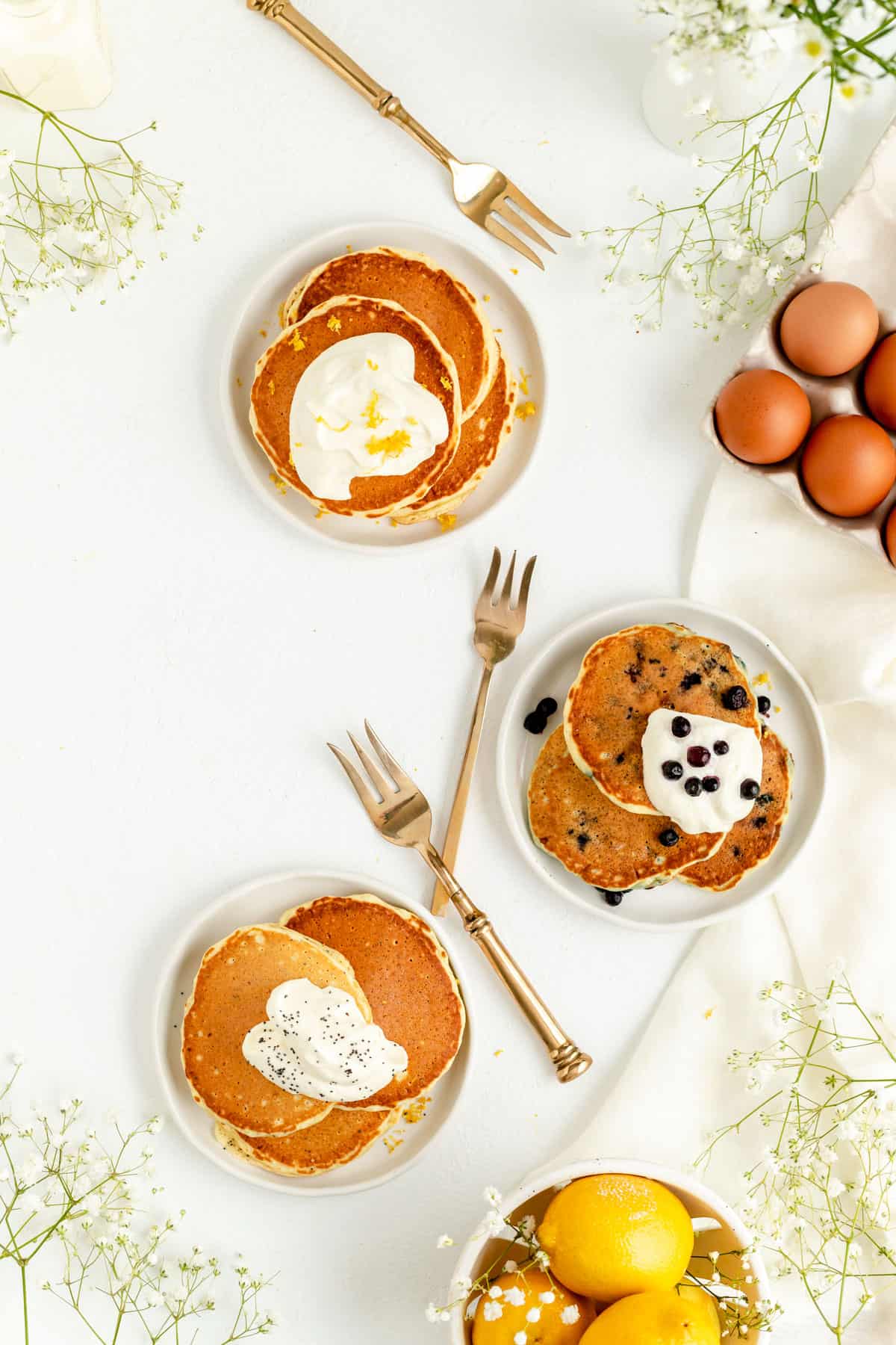 Overhead of lemon blueberry lemon and lemon poppyseed pancakes on separate plates.