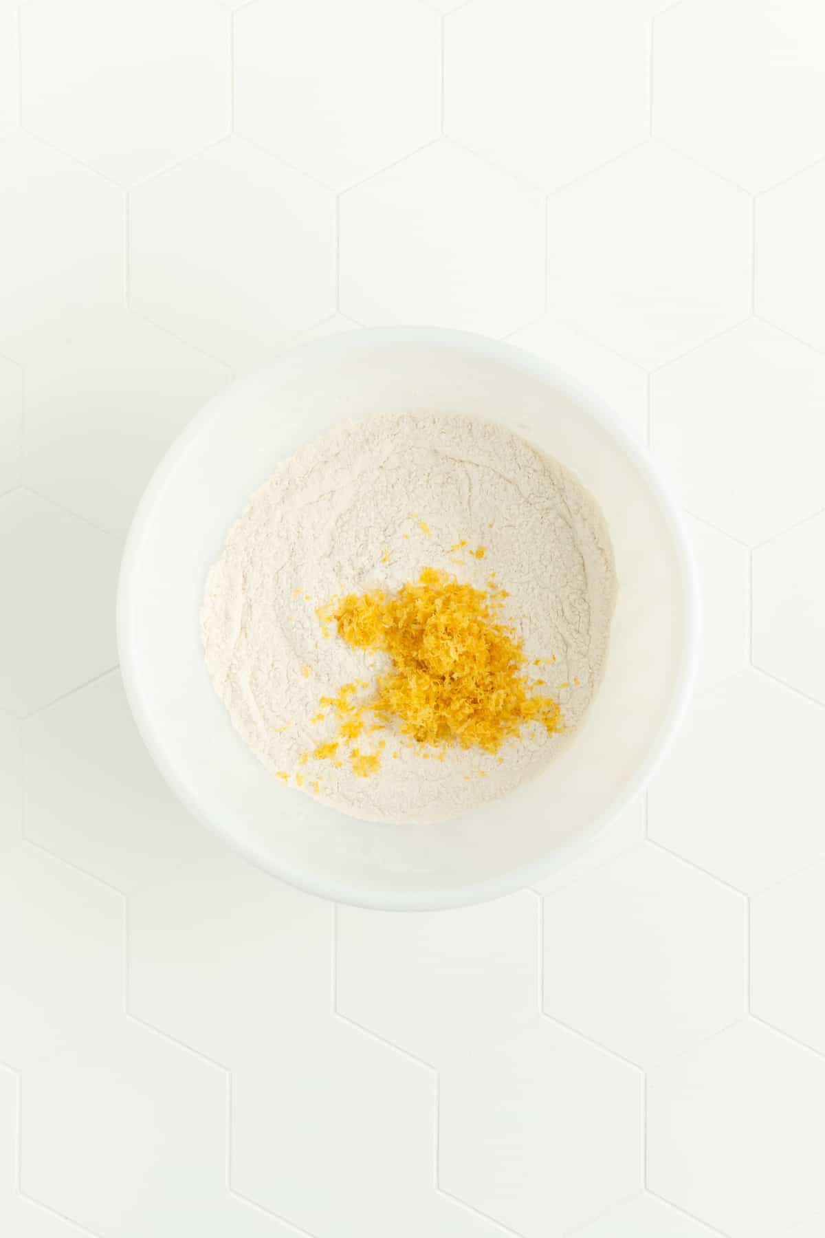 Dry ingredients and lemon zest for lemon pancakes in white mixing bowl.