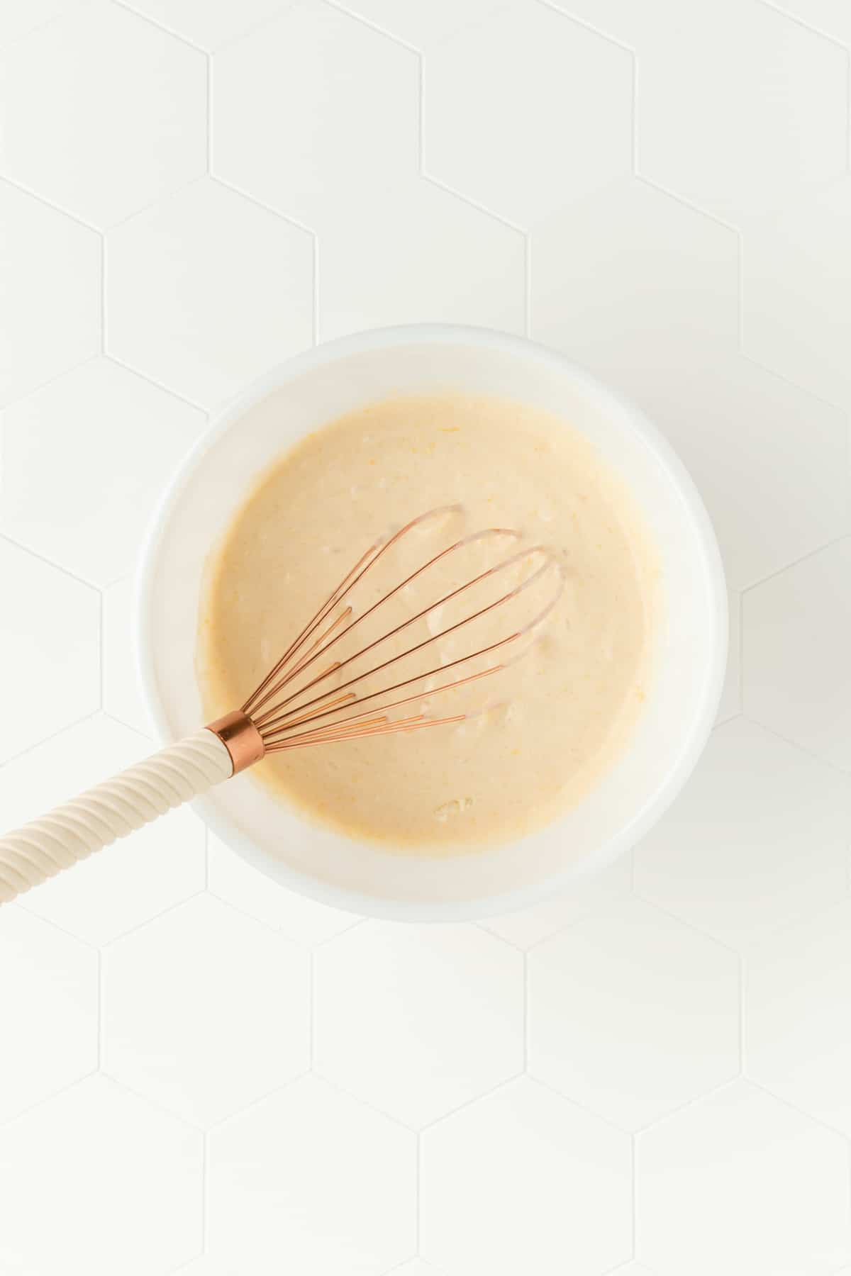 Lemon pancake batter in white mixing bowl with copper and Ivory whisk.