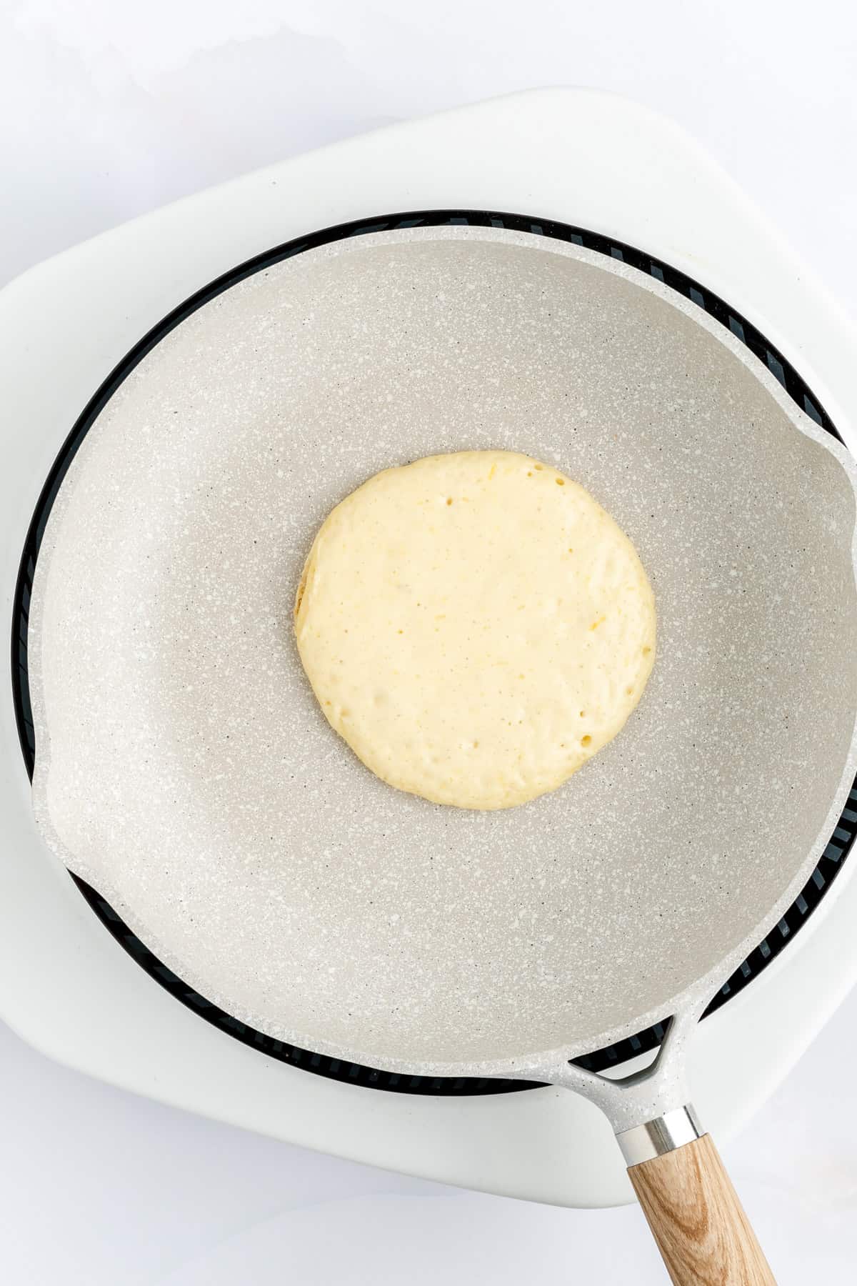 Raw matte top of a lemon pancake cooking in gray pan on white induction stove.
