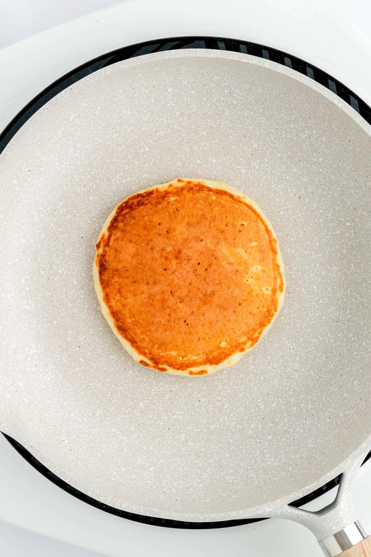 Flipped cooked golden-brown top of lemon pancake in gray pan on weight induction stove.