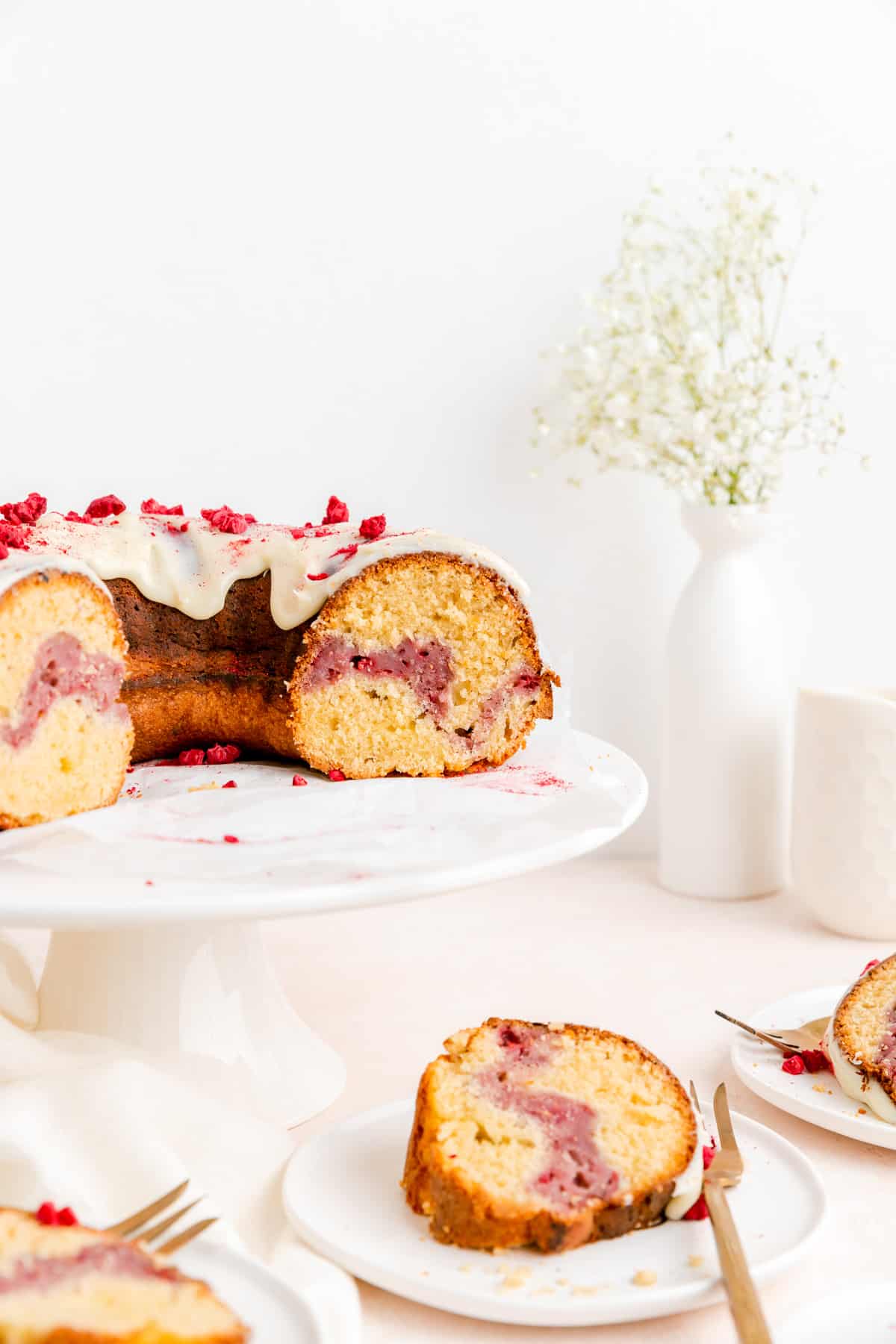 Cut Raspberry white chocolate Bundt cake on white cake stand with slices below on plates.